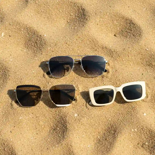 Three pairs of GlamWorlds sunglasses on golden sand – luxury eyewear summer collection